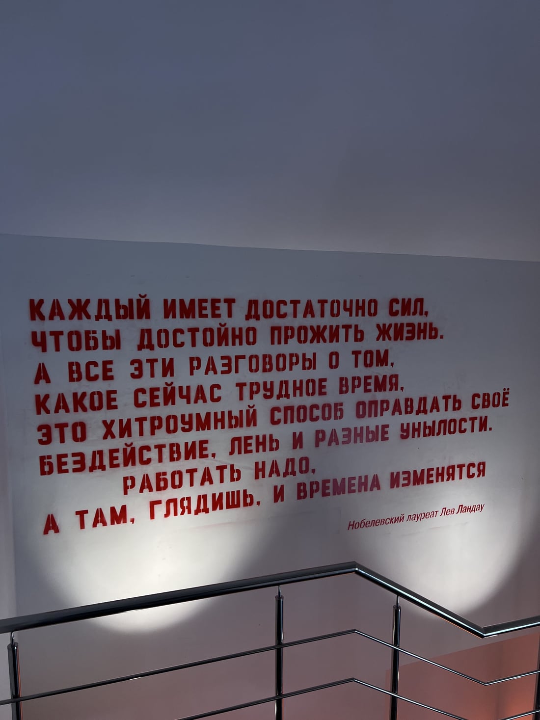 Стена лестницы в офисе с крупной надписью: цитата Льва Ландау о том, что работать надо, а разговоры о трудном времени это способ оправдать бездействие